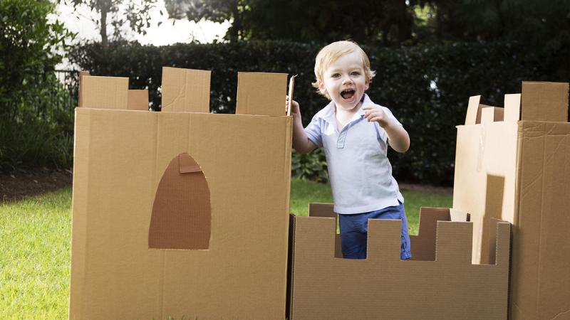 young boy plays in the yard with a castle made from cardboard box
