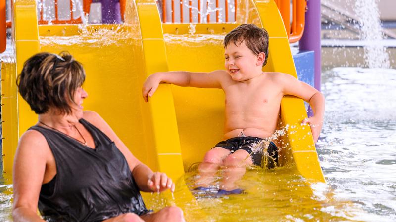 A mother and son playing on a water slide.