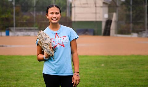 A smiling photo of Arielle with on a softball glove on. 