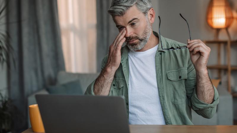 A man rubs his eyes after removing his glasses.
