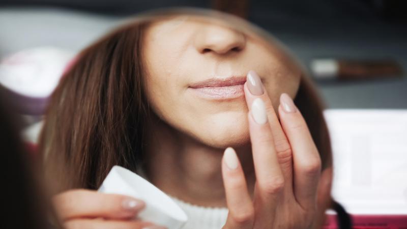A woman putting on lip balm in a mirror.
