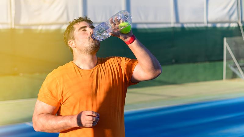 A man drinking a beverage after exercising outdoors.