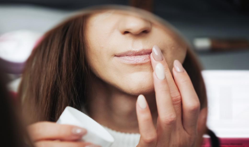 A woman putting on lip balm in a mirror.